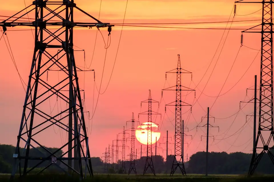 High-voltage transmission towers and power lines silhouetted against a sunset sky.