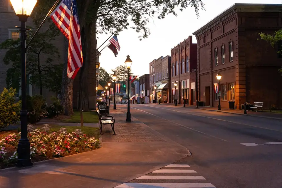 A small-town main street lined with storefronts and American flags at dusk.