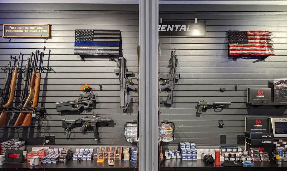 Handguns displayed in a glass case along a gun shop counter.