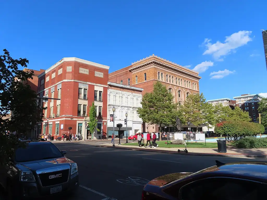 Downtown Springfield, Ohio: pedestrians cross a sunlit street lined with historic brick storefronts under a clear blue sky.