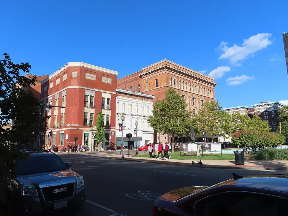 Downtown Springfield, Ohio: pedestrians cross a sunlit street lined with historic brick storefronts under a clear blue sky.
