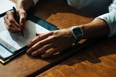 A pair of hands on a desk. Writing on a notepad.