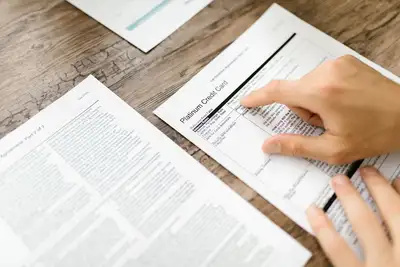 A hand examining the fine print of an agreement on a desk