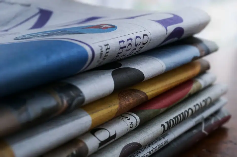 A stack of folded newspapers resting on a wooden table.